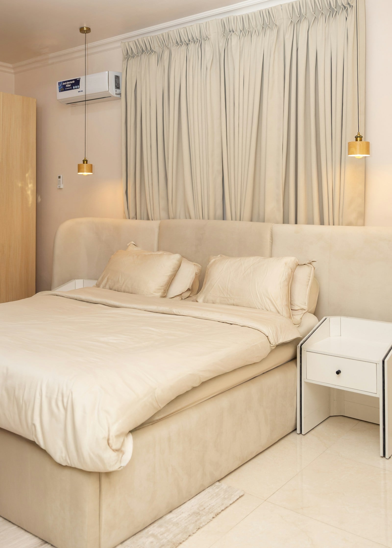 Cream upholstered bed with satin-finish bedding, two brass pendant lights and floor-length curtains
