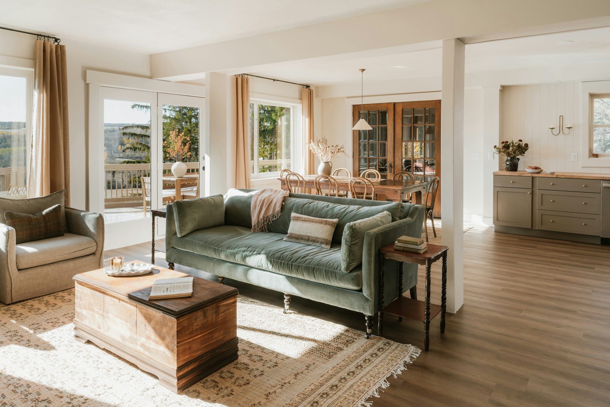 Open-plan living room with a green velvet sofa, a timber trunk coffee table, a patterned rug and a dining area beyond