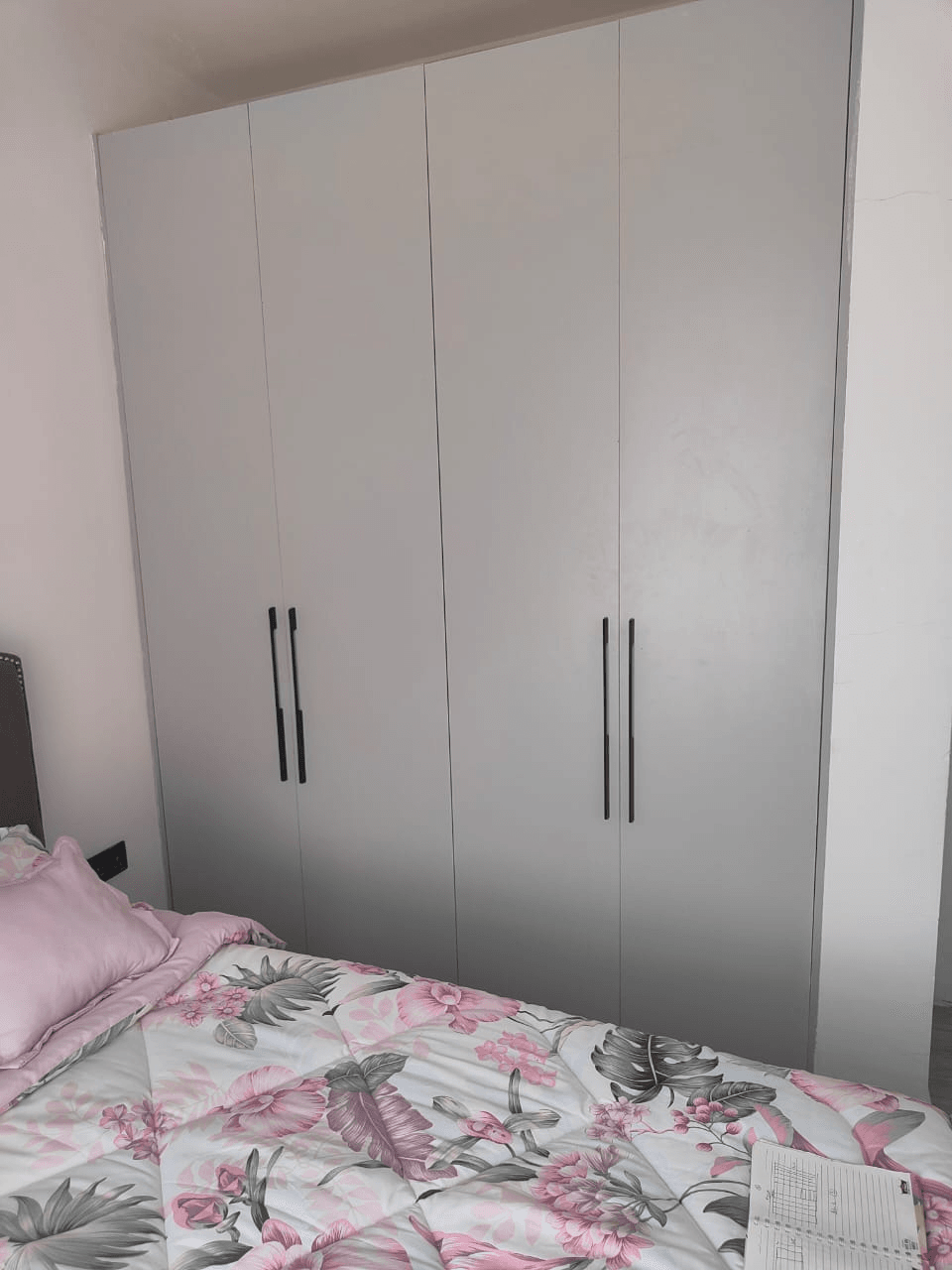 Floor-to-ceiling fitted wardrobe with four grey doors and long black vertical handles beside a bed with floral bedding
